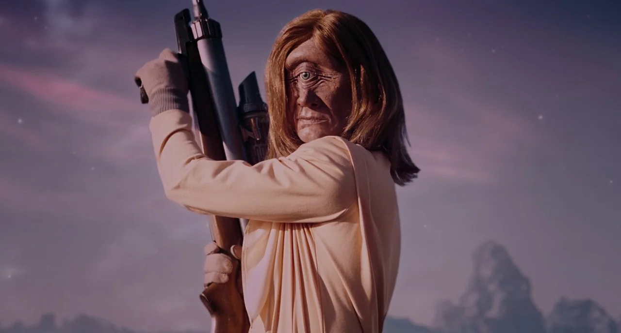 Gentlemen Broncos (2009) movie still: medium — A cyclopean figure stands in a vast, desolate landscape under a purple-tinted dusk sky. The subject…