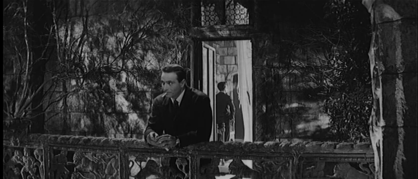 I Vampiri (1957) movie still: medium — An outdoor stone terrace featuring a heavily textured balustrade with ornate carvings. A man stands at the…
