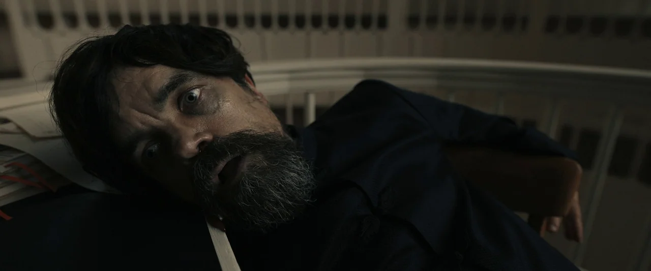 The Hunger Games: The Ballad of Songbirds & Snakes (2023) movie still: closeup — A man lies prone on a dark desk against a curved white railing…