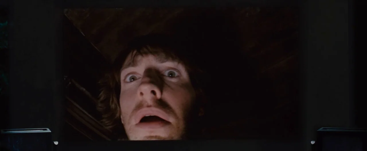 The Cabin In The Woods (2012) movie still: A character is framed by the darkness of a cramped, enclosed space as they look down into an unseen area.…