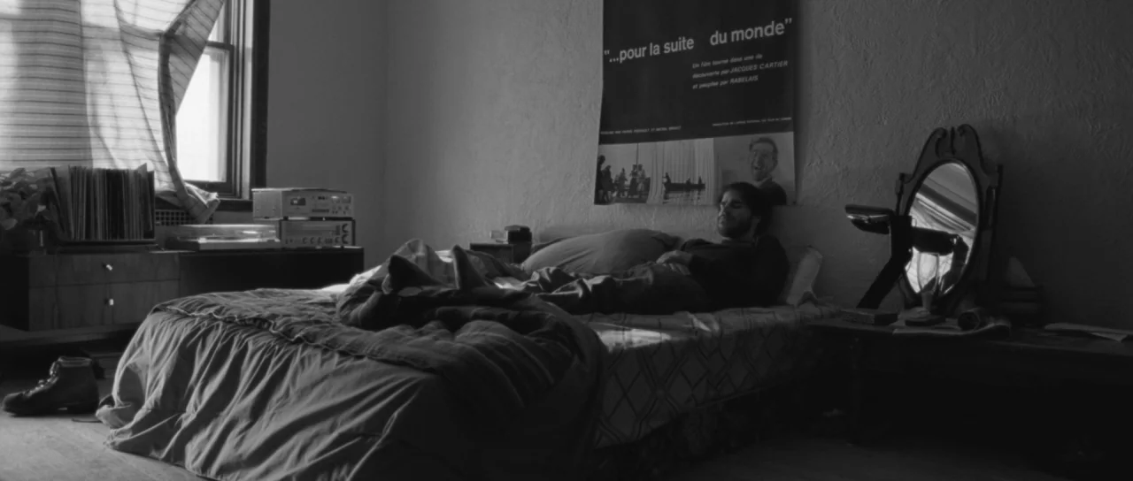 Polytechnique (2009) movie still: medium — A bedroom contains a messy bed and a wall poster titled Pour la suite du monde. A man lies on the bed…