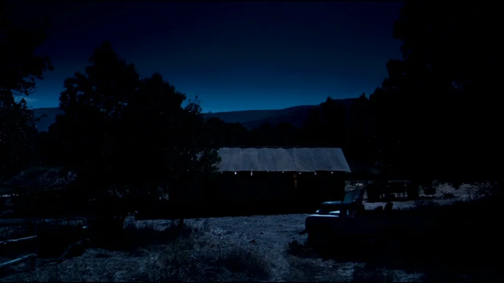 Che Part 2 (Guerrilla) (2008) movie still: establishing — A rural cabin sits under a dark night sky with silhouettes of surrounding trees. A single…