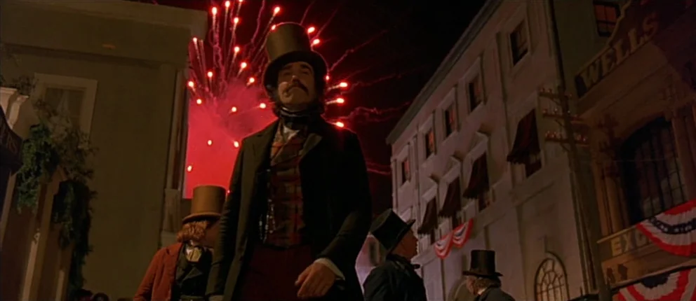 Gangs of New York (2002) movie still: fullbody — A 19th-century street with period architecture is lit by bright red firework explosions overhead. A…