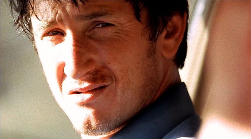 U-Turn (1997) movie still: closeup — A close-up shot showing a man inside a vehicle illuminated by bright natural light. The man looks forward…