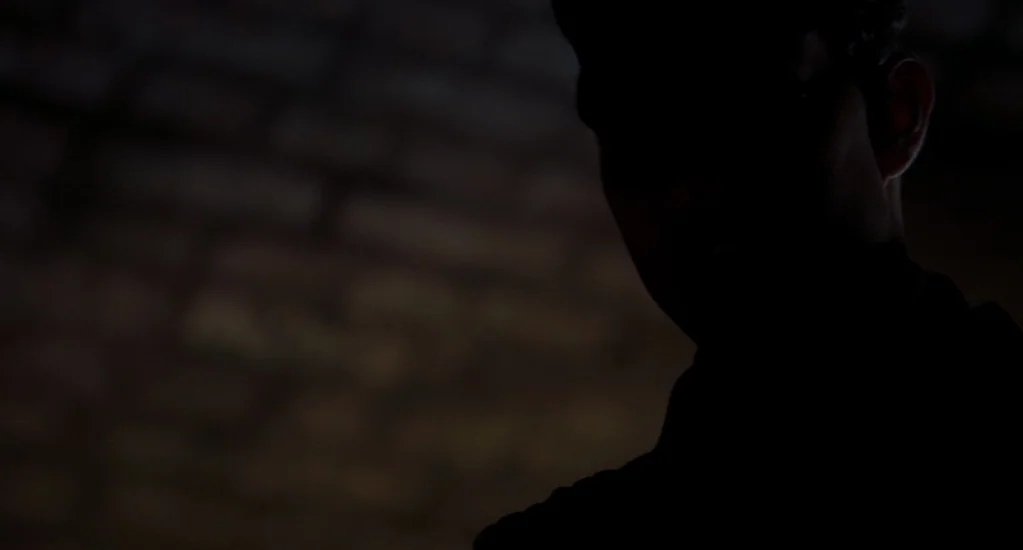 Valkyrie (2008) movie still: closeup — A dark space features a brick wall illuminated by a low-level light source. A person is seen in profile…