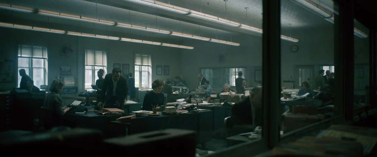 Boston Strangler (2023) movie still: wide — A spacious 1970s open-plan newsroom contains multiple rows of metal desks and file cabinets. Various…