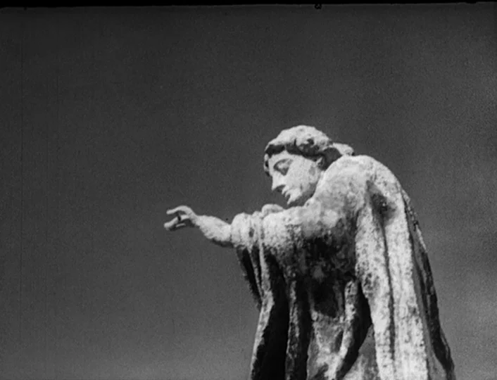 The White Sheik (1952) movie still: medium — A stone statue stands against an empty, overcast sky background. The figure wears a long robe and…