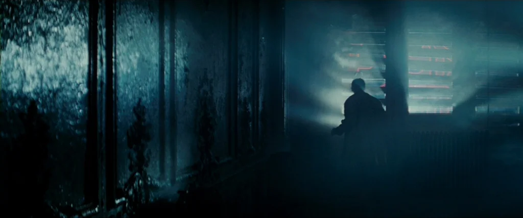 Blade Runner (1982) movie still: wide — A dimly lit, narrow corridor features ornate wall molding and thick, hazy atmosphere. A lone man stands in…