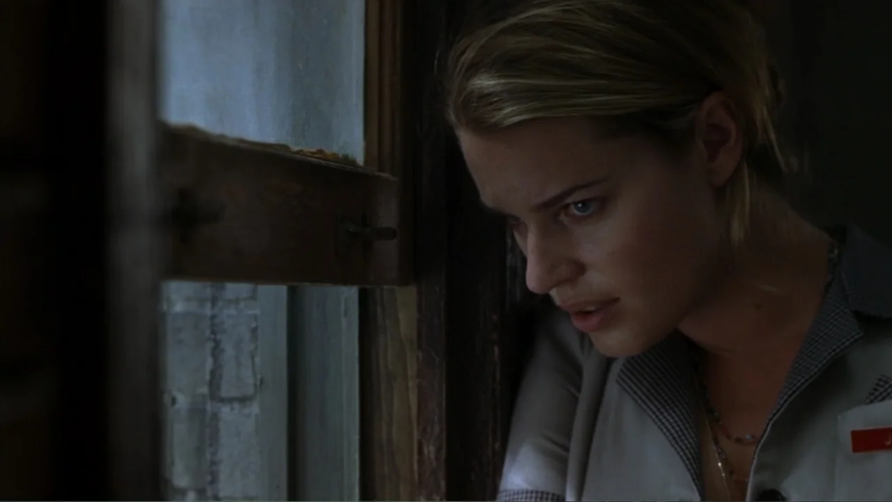 The Punisher (2004) movie still: closeup — A dark indoor space with a window frame visible on the left side. A young woman wearing a uniform stands…