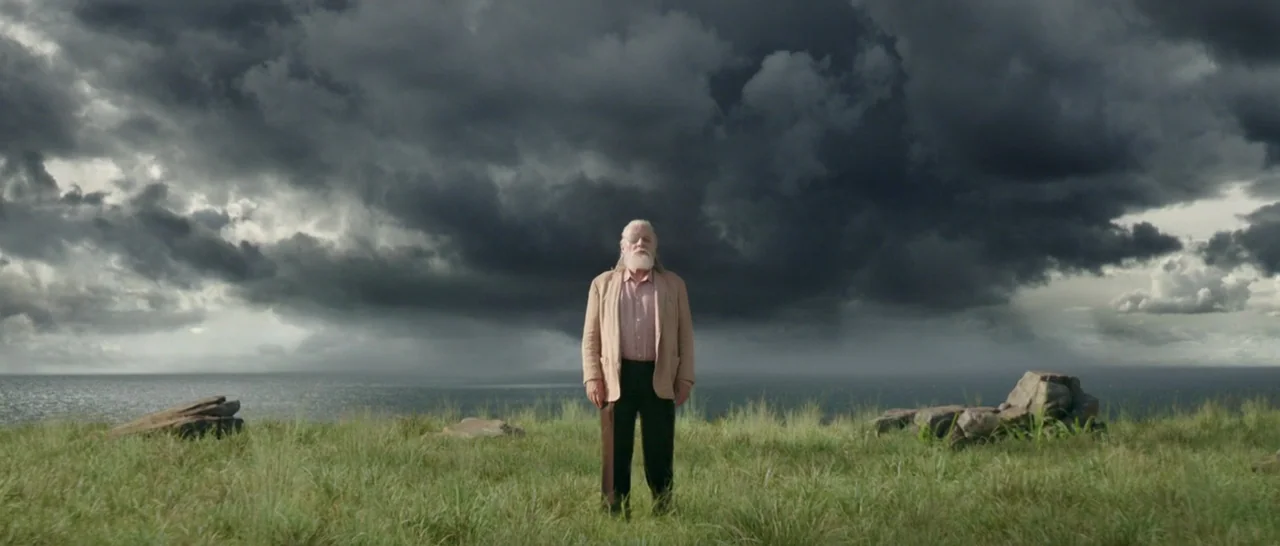 Thor: Ragnarok (2017) movie still: fullbody — A man stands in a grassy field on a cliff overlooking the ocean. Heavy dark storm clouds fill the vast…