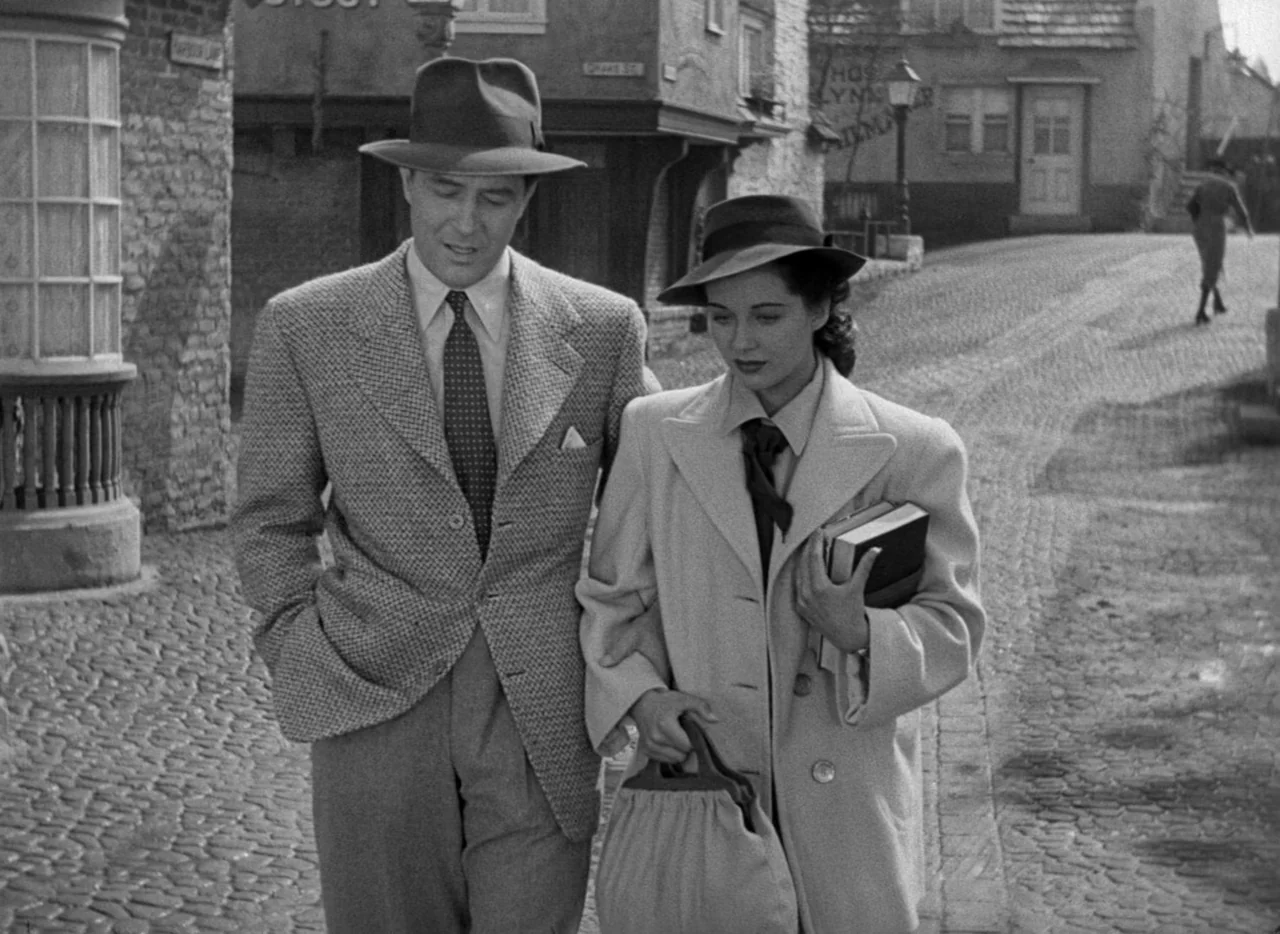 The Uninvited (1944) movie still: medium — A quiet cobblestone street features historic timber-framed buildings and a streetlamp in the background.…