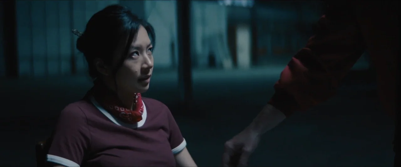 Stalker (2020) movie still: medium — An dimly lit, expansive industrial space with dark, blurred structural features in the background. A woman in a…