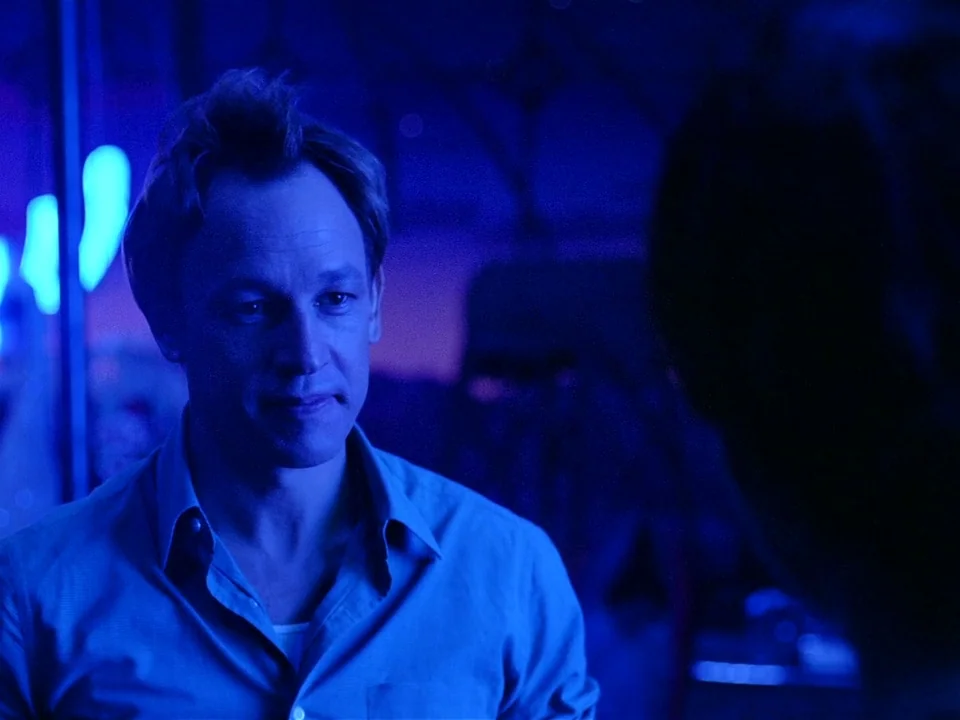One From The Heart (1982) movie still: medium — A man stands in a dark space filled with intense blue neon light. He is listening to a person whose…