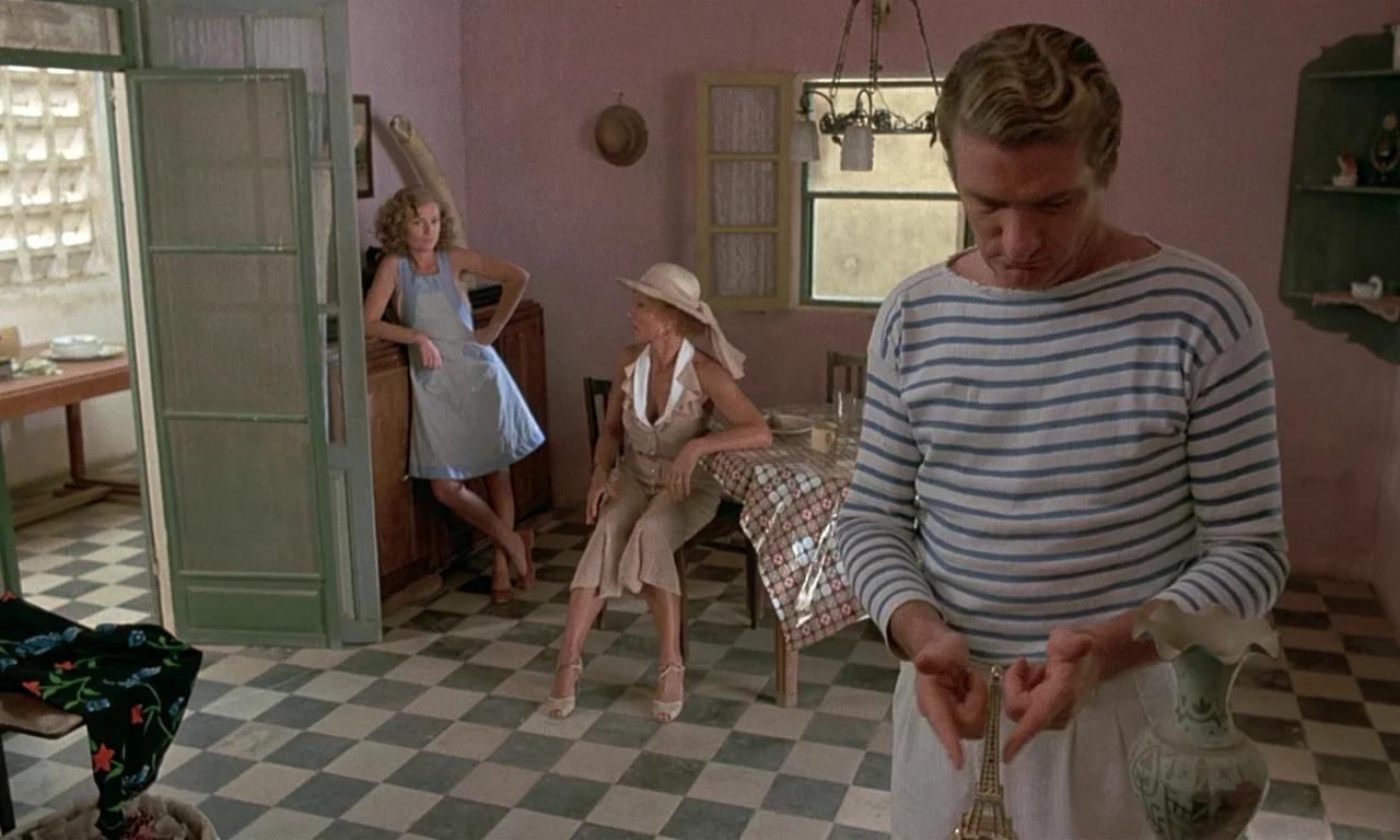 Coup De Torchon (1981) movie still: medium — A domestic interior with pale pink walls and a black and white checkerboard floor. A man holds a small…