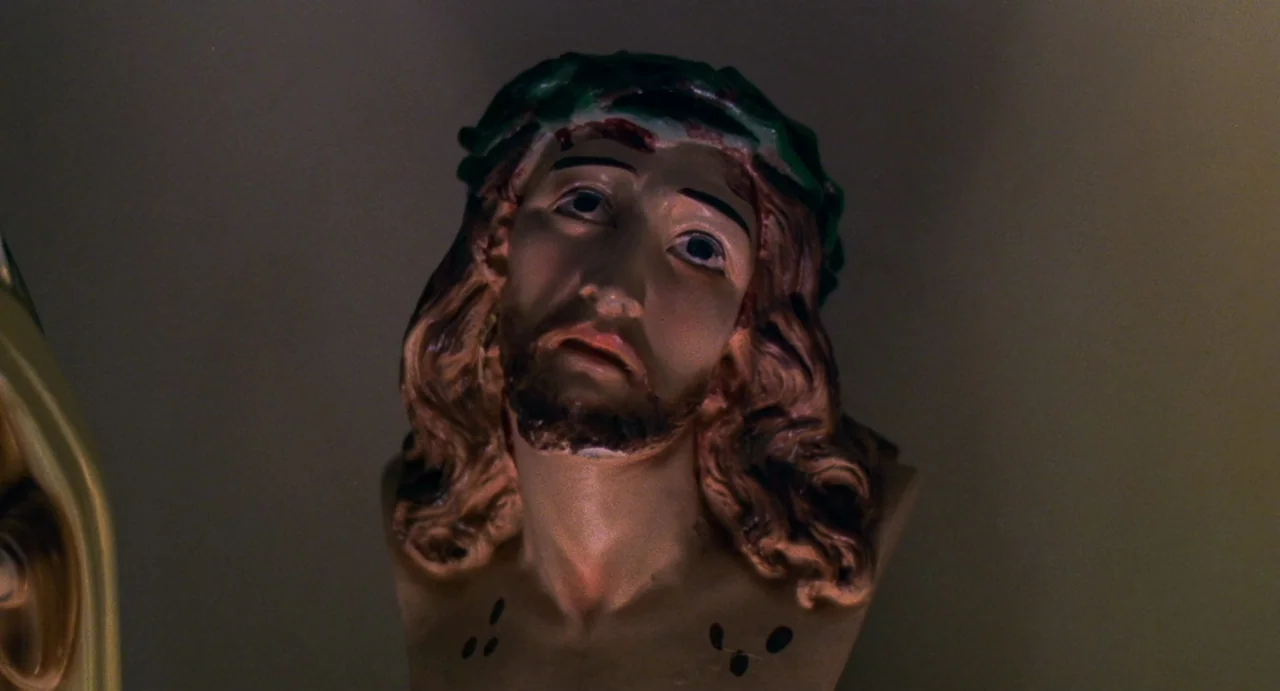 God Told Me To (1976) movie still: closeup — A close-up view of a ceramic bust of a man with a crown. The statue is against a dark, featureless…