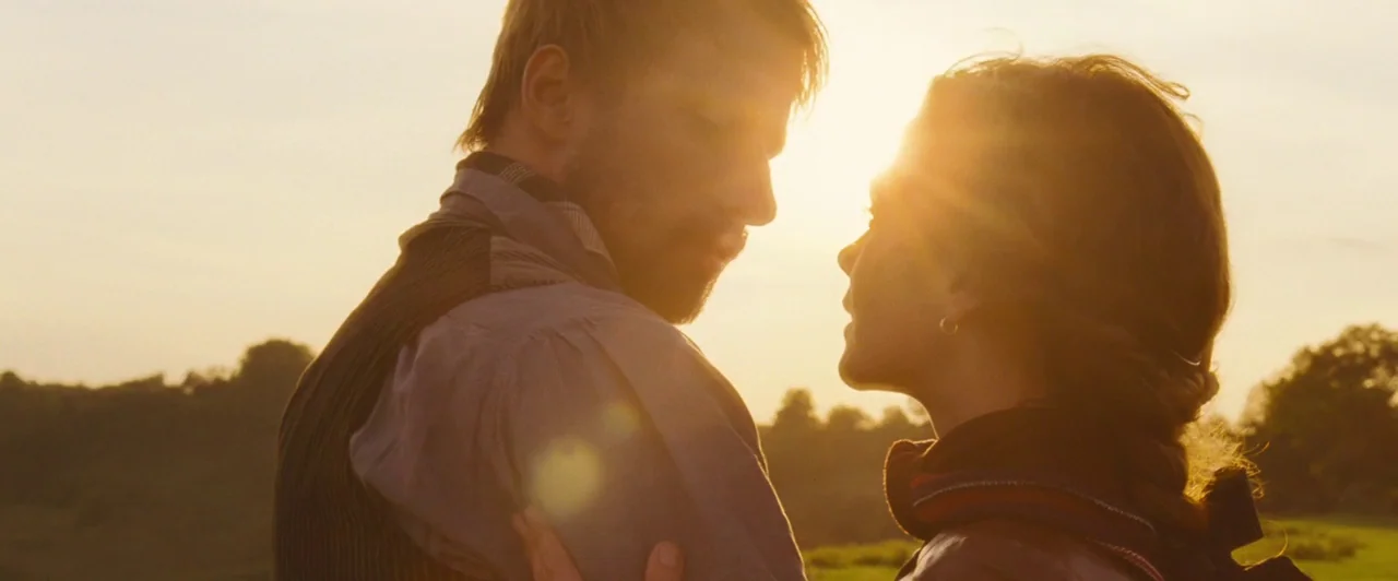 Far from the Madding Crowd (2015) movie still: medium — An open rural field during golden hour with silhouettes of trees in the distance. A man and…
