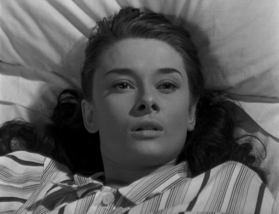 Roman Holiday (1953) movie still: closeup — A woman lies on a white pillow in a sparsely decorated room. She stares upward with a relaxed expression…