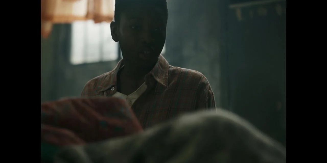 Autumn Beat (2022) movie still: medium — A dimly lit room features a window with thin curtains and textured walls. A teenage boy stands in the…