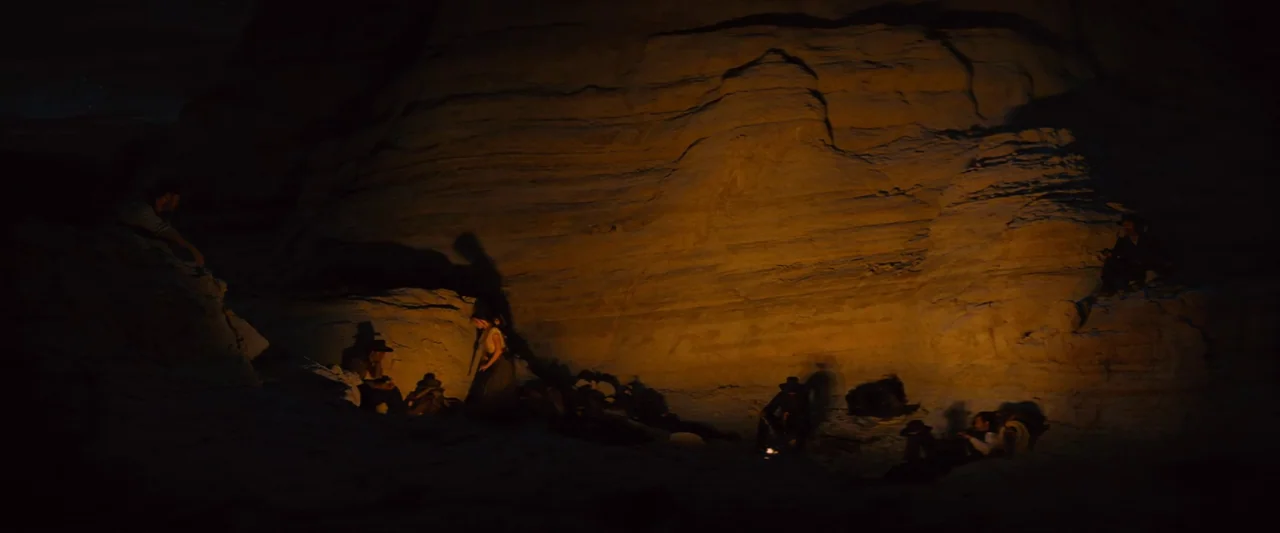 The Magnificent Seven (2016) (2016) movie still: wide — A group of people gathers around a small campfire inside a dark rock canyon. Long shadows…