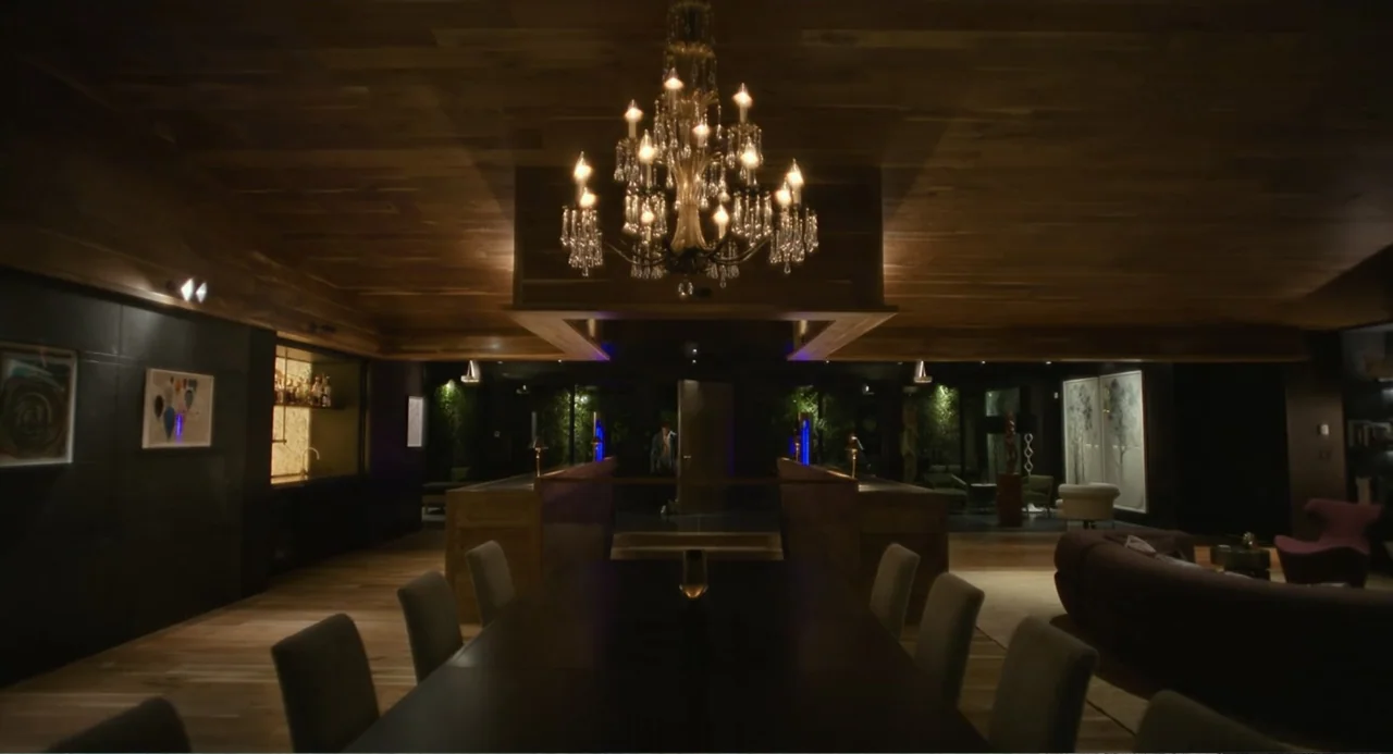 Turtles All the Way Down (2024) movie still: wide — A spacious high-end modern interior features a long dining table and wooden ceilings. A large…
