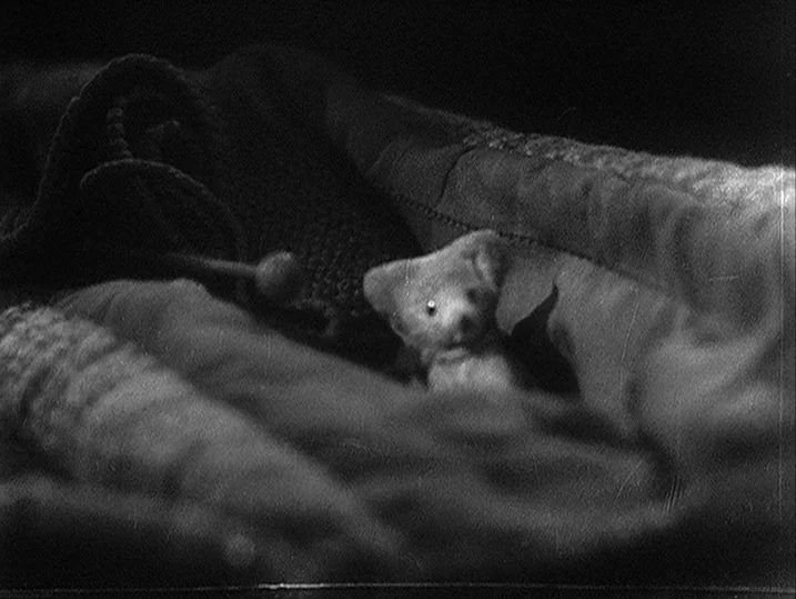 One Wonderful Sunday (1947) movie still: closeup — A small plush toy bear sits tucked into layers of thick, folded bedding. The scene is captured in…