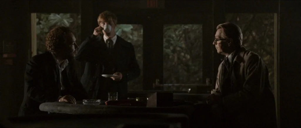 Tinker Tailor Soldier Spy (2011) movie still: medium — A dimly lit, wood-paneled bar interior features three men at a circular table. One man stands…