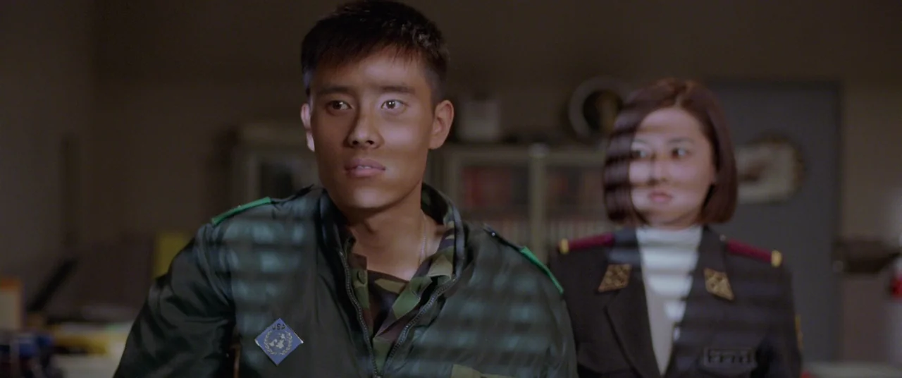 Joint Security Area (2000) movie still: medium — An interior space features two individuals in military dress uniforms standing before window…