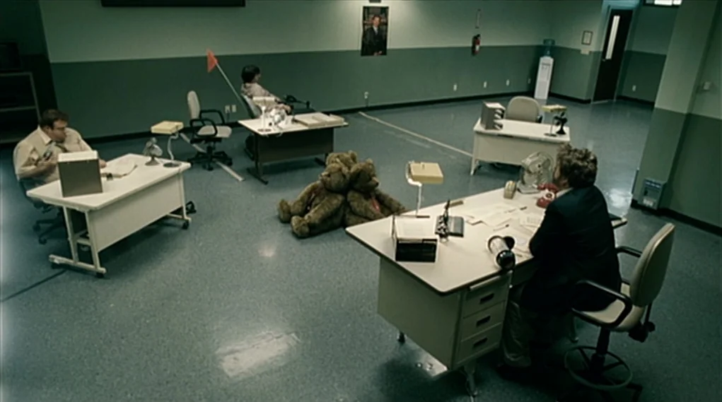 Visioneers (2008) movie still: wide — A spacious, minimalist office with pale green walls and a gray speckled floor. Three men work at individual…