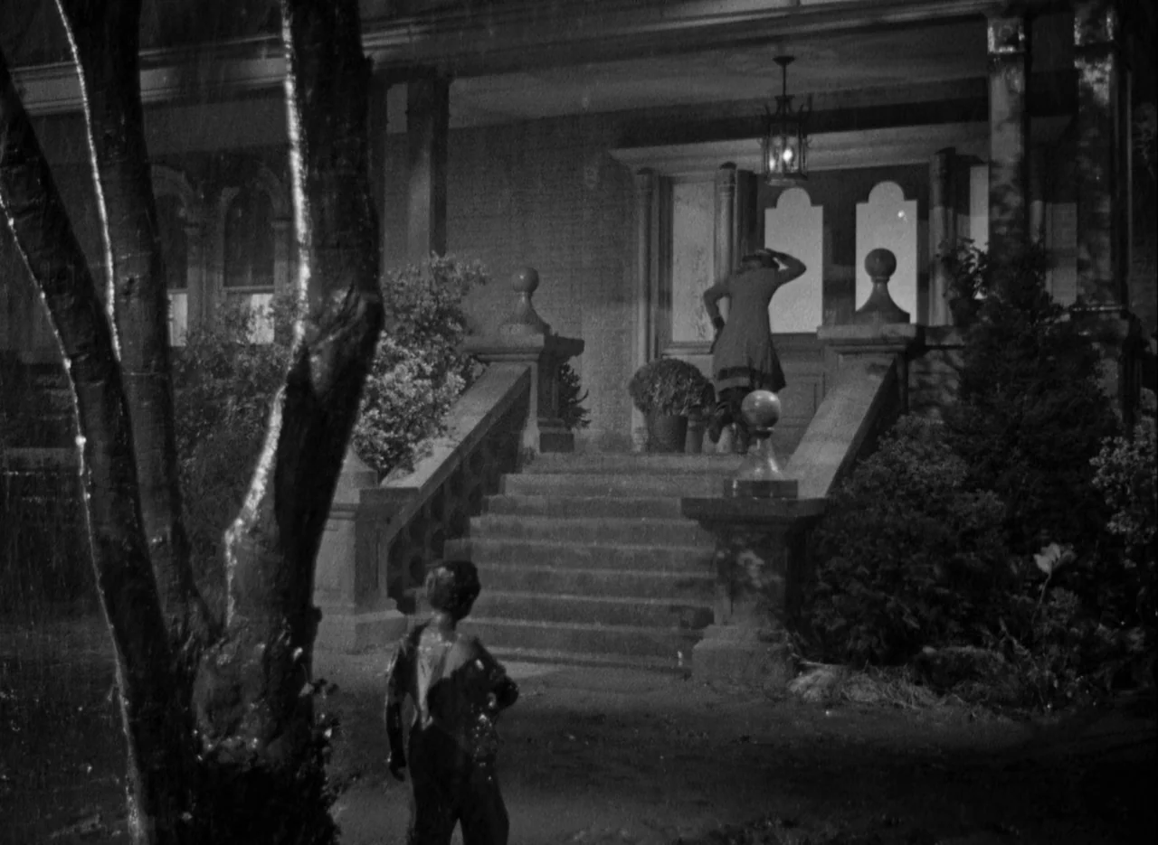 The Spiral Staircase (1946) movie still: wide — A nighttime scene of a residential home exterior with a stone staircase and porch. A woman in a coat…