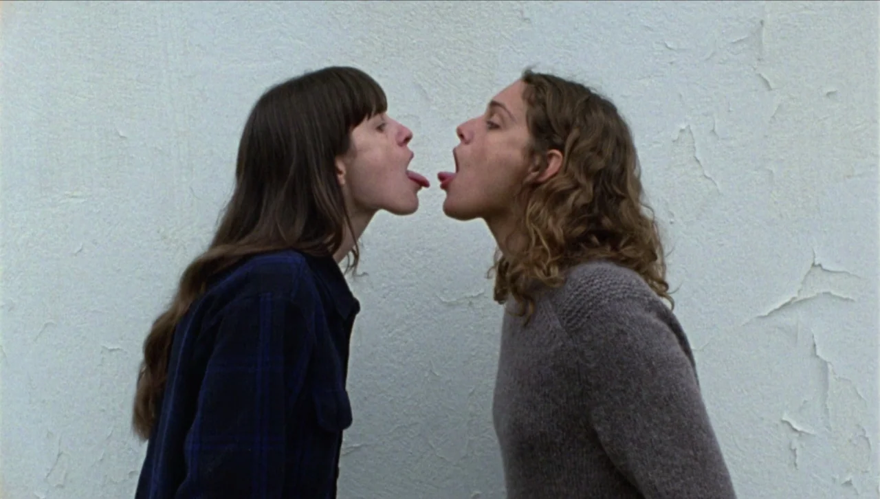 Attenberg (2010) movie still: medium — Two women stand in profile against a plain, textured white painted wall. They are positioned closely…