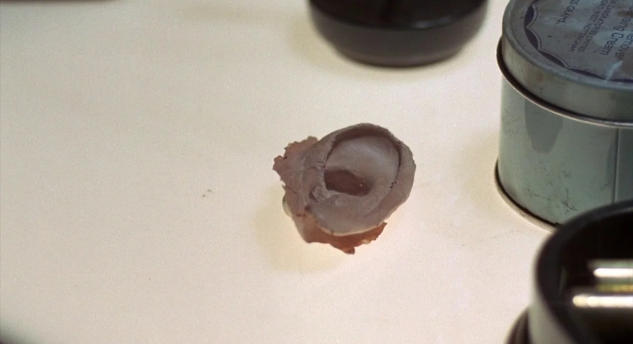 The Abominible Dr. Phibes (1972) movie still: closeup — A light-colored vanity surface holds a prosthetic human ear next to a tin container. The…