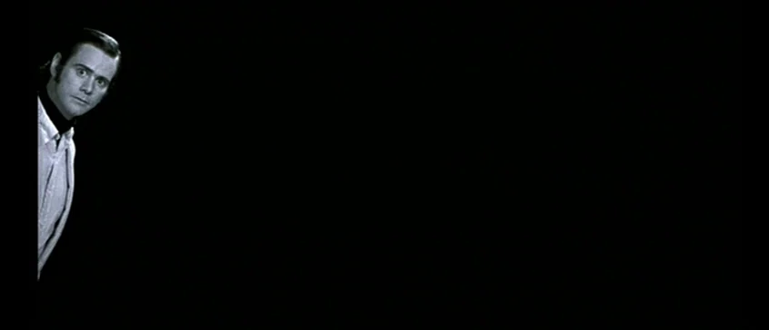Man On The Moon (1999) movie still: medium — A man partially enters the frame from the left side against a solid black background. He looks directly…