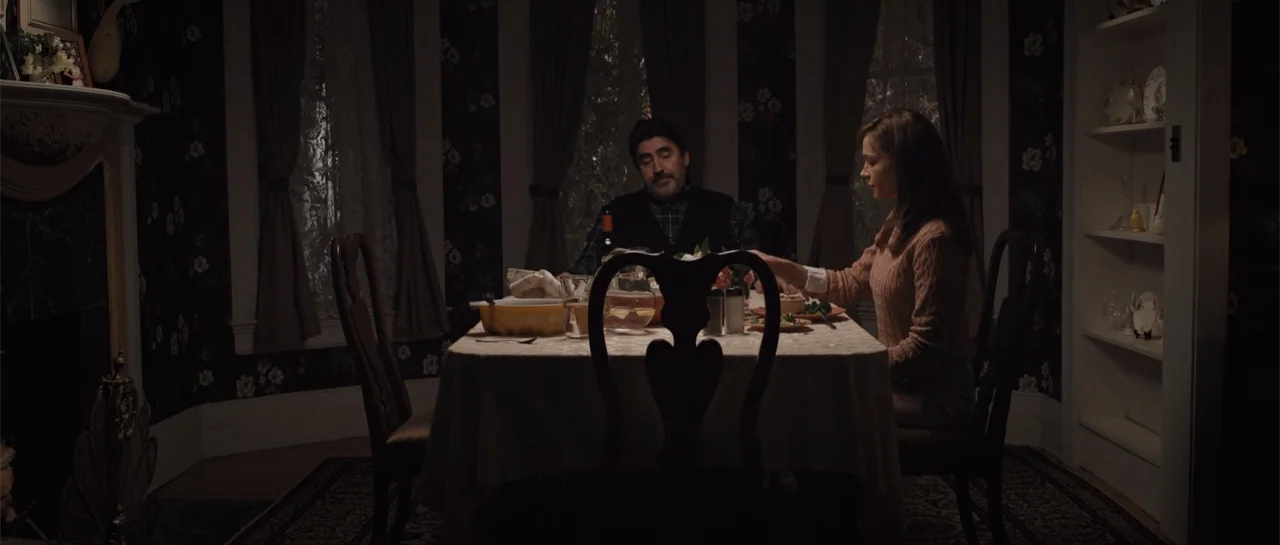 The Truth About Emanuel (2013) movie still: medium — A dark dining room features floral wallpaper and windows draped in lace curtains. A man and…