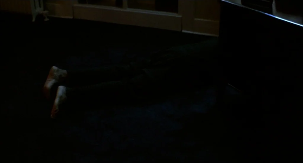 Bubba Ho-Tep (2002) movie still: medium — A dark carpeted surface with a person lying prone in the dim shadow. Only the person's feet and lower legs…