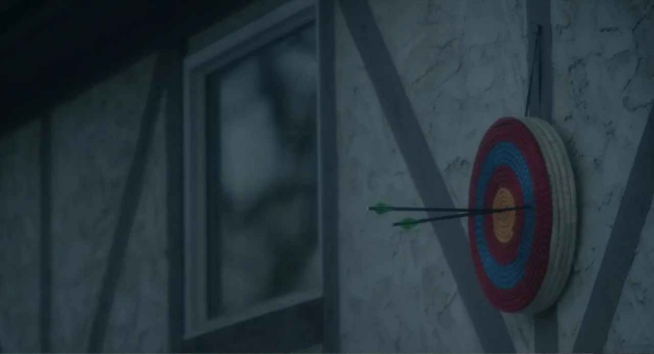 Orphan: First Kill (2022) movie still: medium — A stucco wall with timber framing features a window and an archery target. Two arrows are stuck…