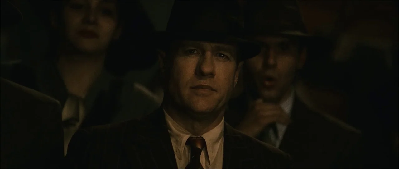 The Black Dahlia (2006) movie still: medium — A group of people wearing 1940s-style hats stand in a dimly lit, shadowy environment. A man in a…