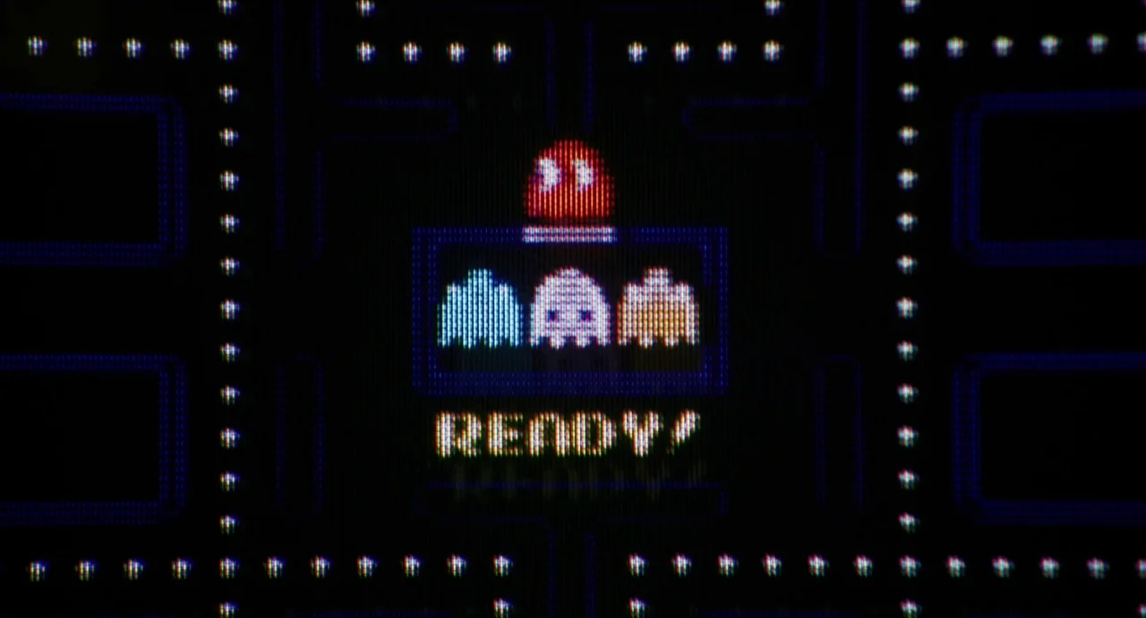 Relaxer (2018) movie still: closeup — A close-up view of a classic video game screen shows ghosts inside a small box. The word READY! is displayed…