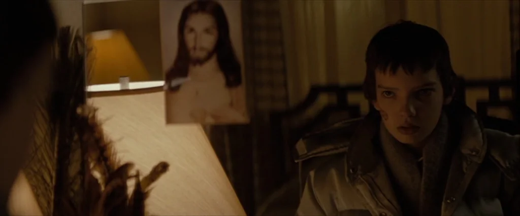Let Me In (2010) movie still: medium — A dark indoor space featuring a portrait of Jesus attached to a lamp. A teenage boy with short brown hair…