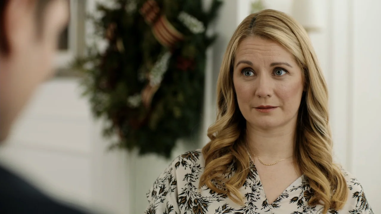 Christmas in Washington (2003) movie still: medium — A bright living room features a holiday wreath mounted on a white wall. A blonde woman in a…