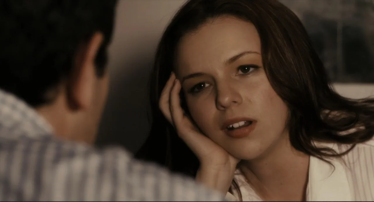 Beyond a Reasonable Doubt (2009) movie still: closeup — An interior space with dim lighting features a woman sitting in conversation with another…