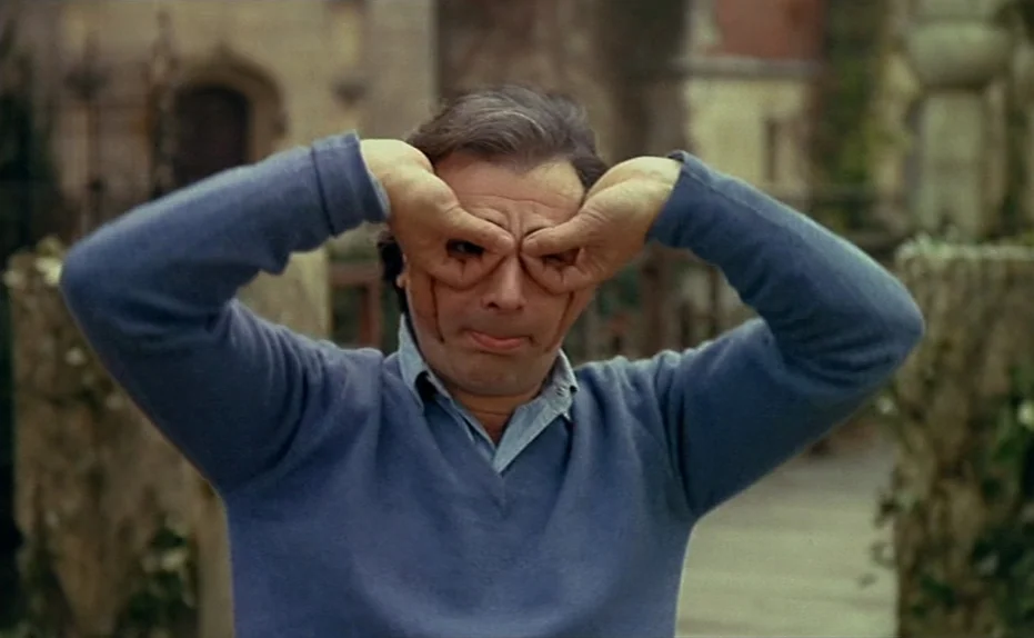 Life Is A Bed of Roses (1983) movie still: medium — A stone courtyard with weathered architecture serves as the backdrop. A man in a blue sweater…