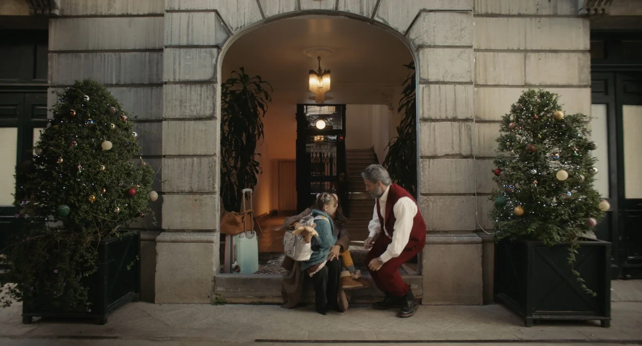 Dating Santa (2023) movie still: fullbody — A stone building archway features two decorated pine trees on either side of steps. An older man…