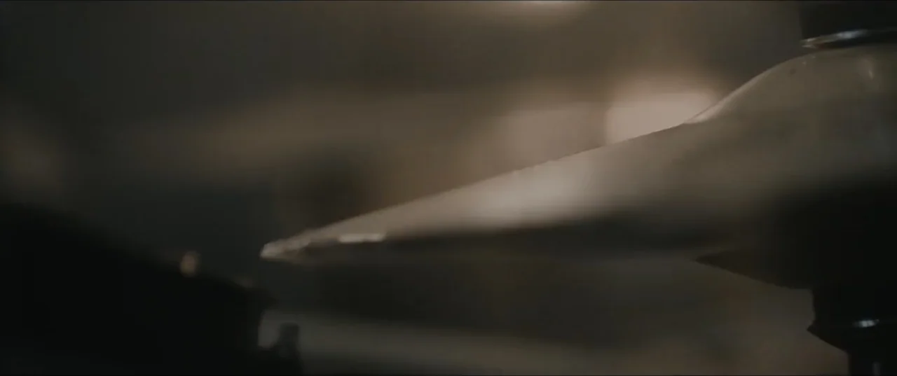 Death to Summer (2021) movie still: closeup — A close-up view of a metal drum cymbal inside a dimly lit room. The metal surface reflects faint light…