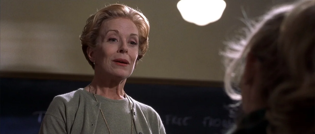 Legally Blonde (2001) movie still: medium — A classroom interior features a black chalkboard with faint writing behind a standing woman. The woman…