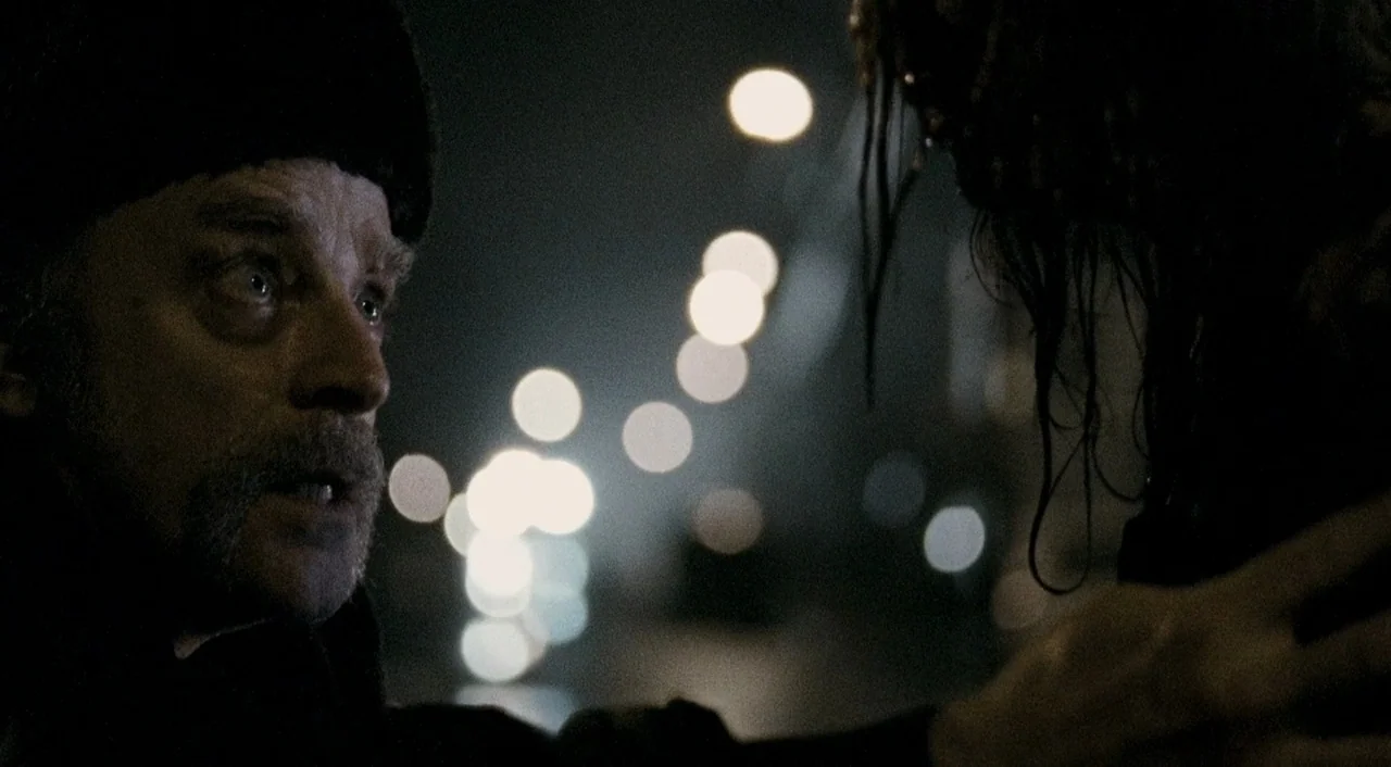 Halloween 2 (2009) movie still: closeup — A dark urban environment at night with blurred bokeh lights in the deep background. An older man in a fur…