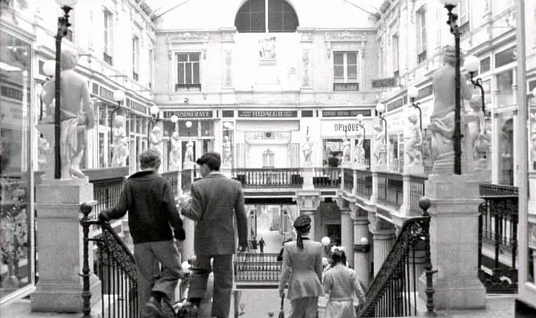 Jacquot de Nantes (1991) movie still: fullbody — A classic 19th-century shopping arcade features ornate neoclassical architecture with statues and…