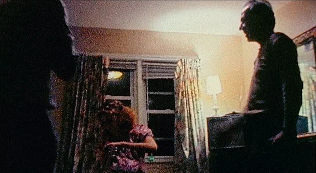 Julien Donkey Boy (1999) movie still: medium — A dark, grain-heavy indoor scene with window curtains and a vintage table lamp. The male subject…