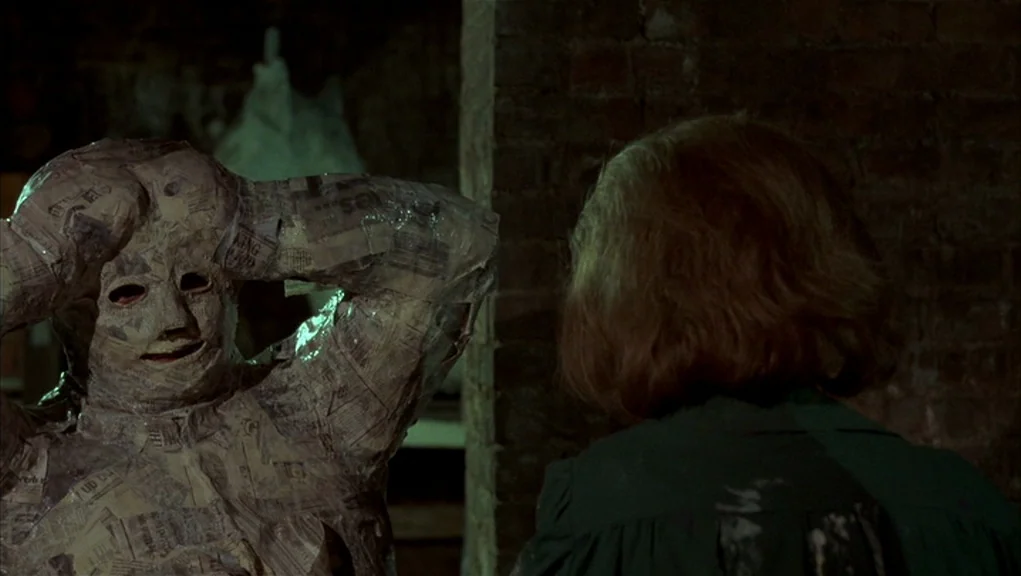 After Hours (1985) movie still: medium — A dimly lit brick basement features a figure wrapped entirely in layers of newspaper. A woman stands in the…