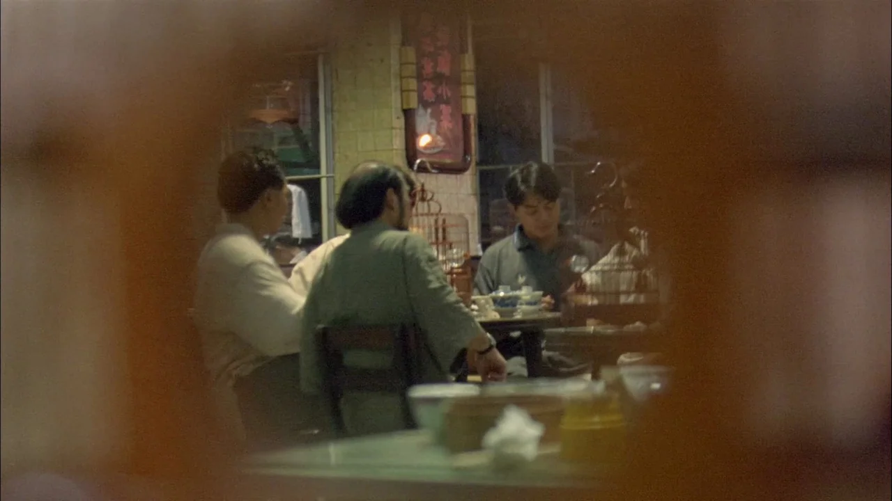 Hard Boiled (1992) movie still: medium — A dimly lit room with vintage decor features men sitting together at a small table. The frame is obscured…