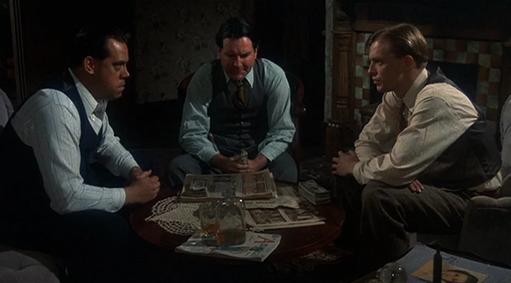 Thieves Like Us (1974) movie still: medium — A dark, wood-paneled room furnished with vintage 1930s decor and patterned wallpaper. Three men sit…